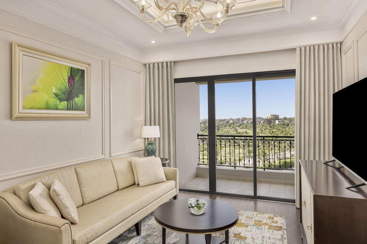 A modern living room with a beige sofa, a round coffee table, a large painting, and a balcony with a city view.