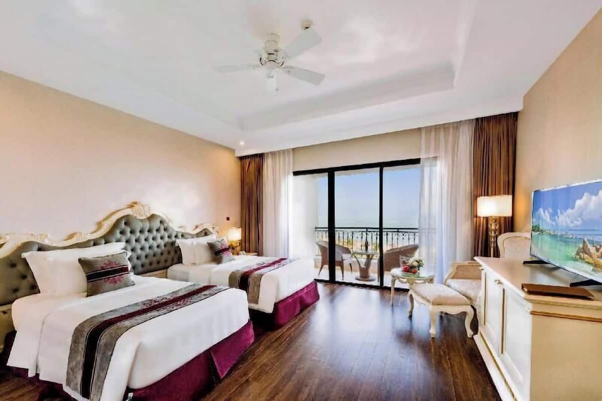 A hotel room with a large bed, a television, a balcony with a view, and a ceiling fan.