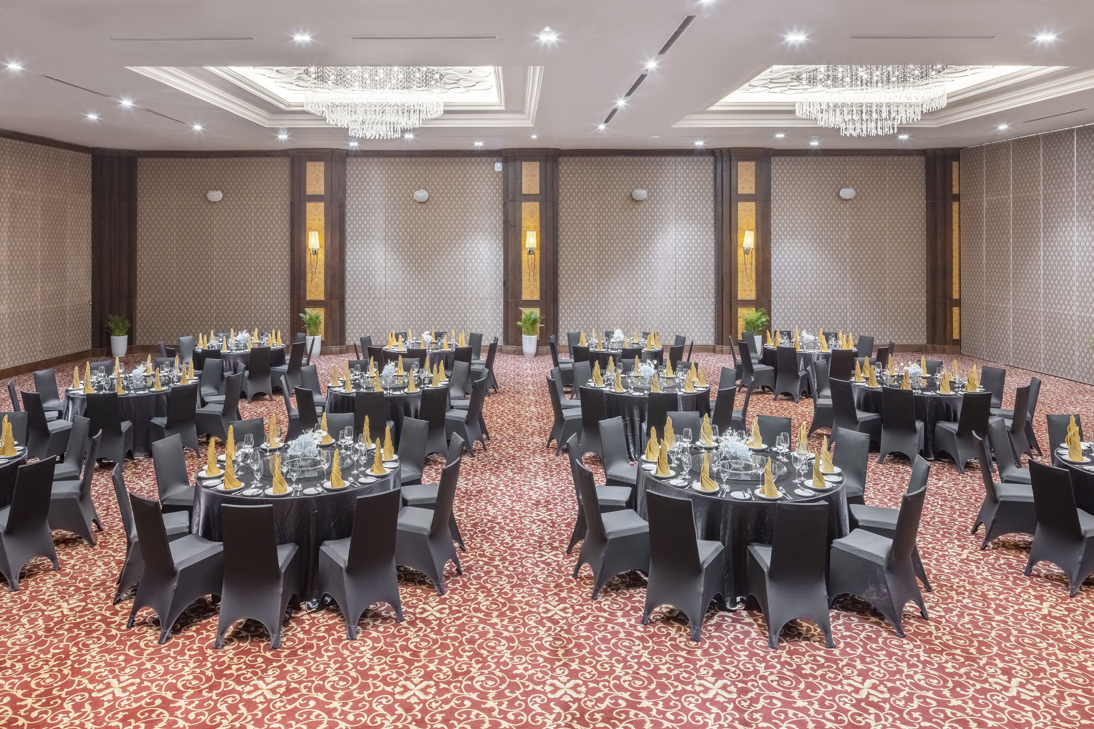 A banquet hall with round tables set for dining, featuring black chairs and a red carpet.