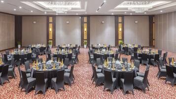 A banquet hall with round tables set for dining, featuring black chairs and a red carpet.