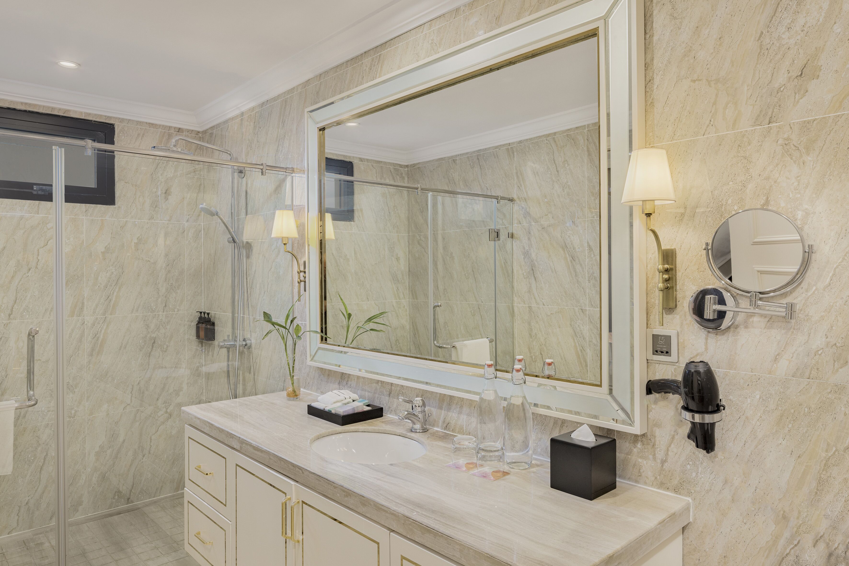 A modern bathroom with a large mirror, a glass shower enclosure, a marble countertop, and a round wall-mounted mirror.