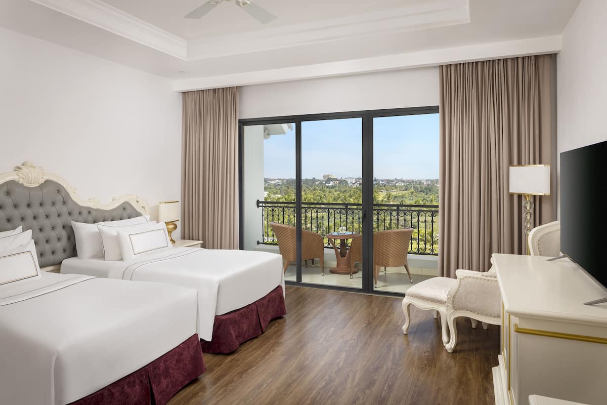 A hotel room with two beds, a balcony with a view, and a desk with a chair.
