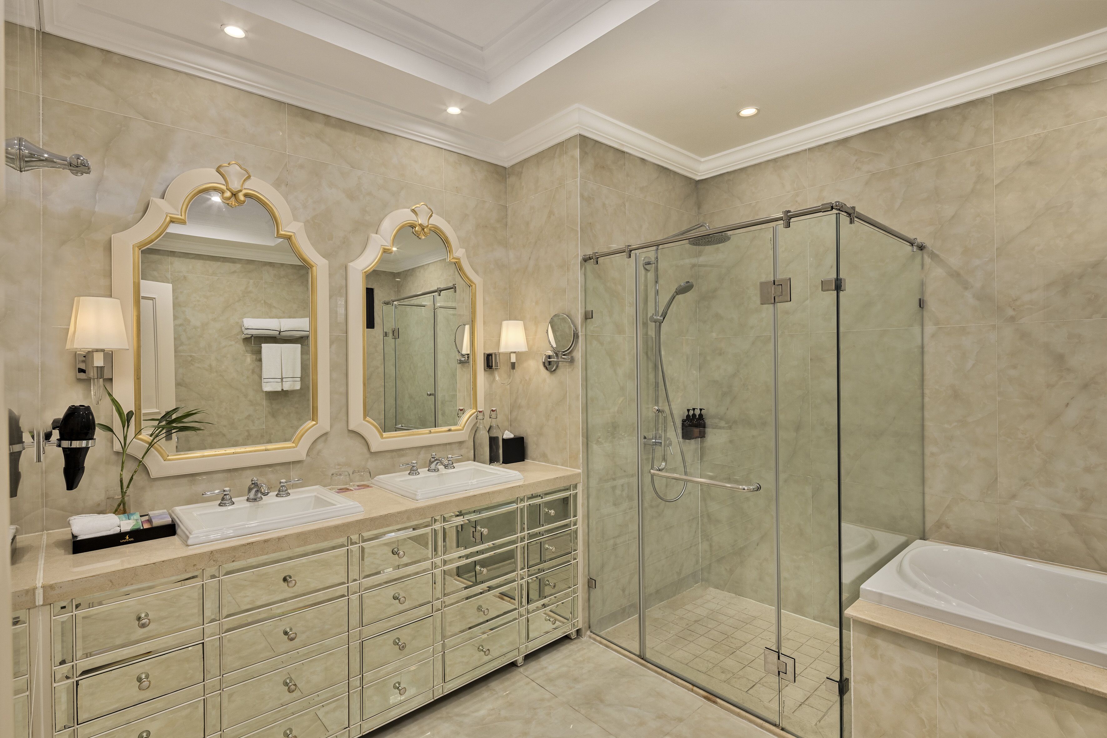 Un baño moderno con ducha envuelta en vidrio, tocador doble y un espejo grande.