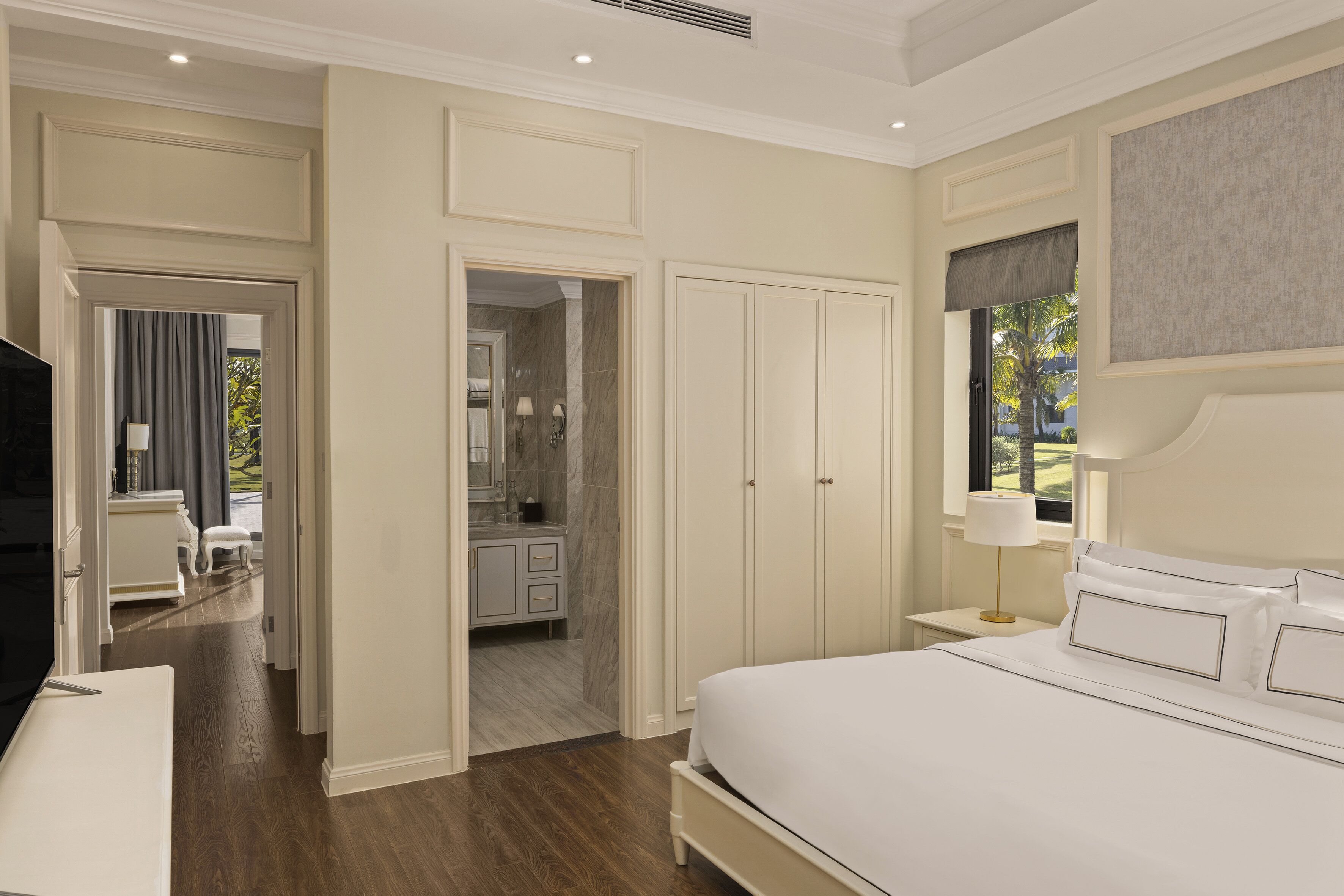 A bedroom with a large bed, a nightstand, a TV, and a bathroom visible through an open door.