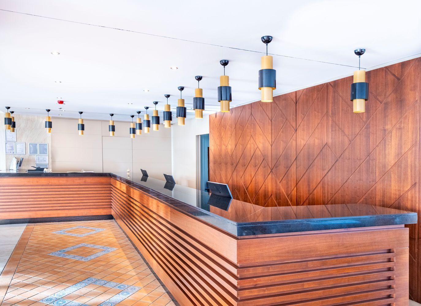 Un área de recepción con un mostrador de madera, varias lámparas colgantes y un piso con diseño.