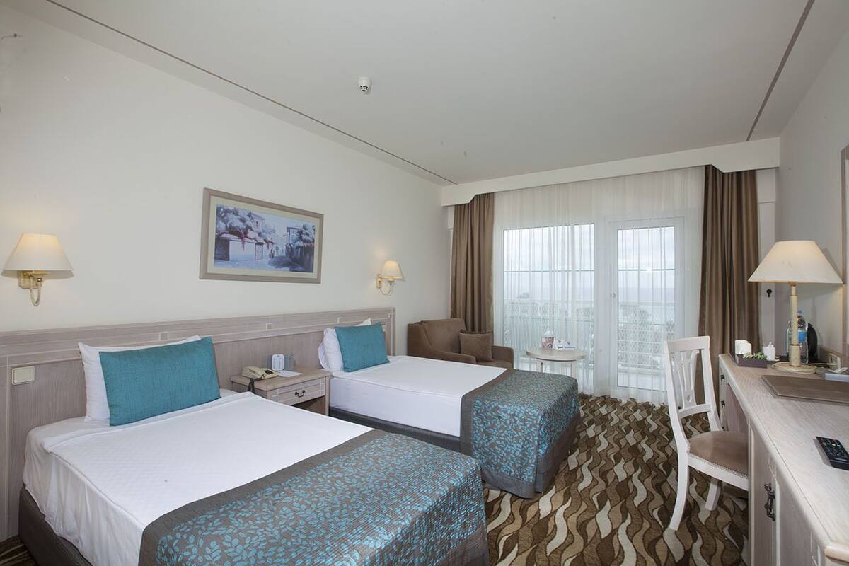 A hotel room with two beds, a desk, a chair, a small table, and a window with curtains.