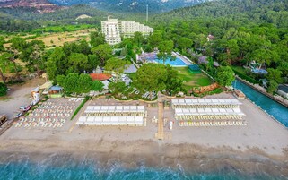 Μια αεροφωτογραφία ενός παραθαλάσσιου θέρετρου με μια πισίνα, ομπρέλες παραλίας και ένα μεγάλο κτίριο στο βάθος.