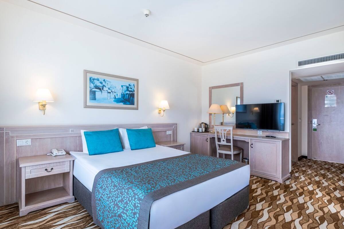 A hotel room with a bed, bedside tables, a desk with a chair, a television, and a door with a sign.