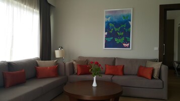 A living room with a grey sofa, red cushions, a white vase with flowers, a lamp, and a painting of butterflies on the wall.