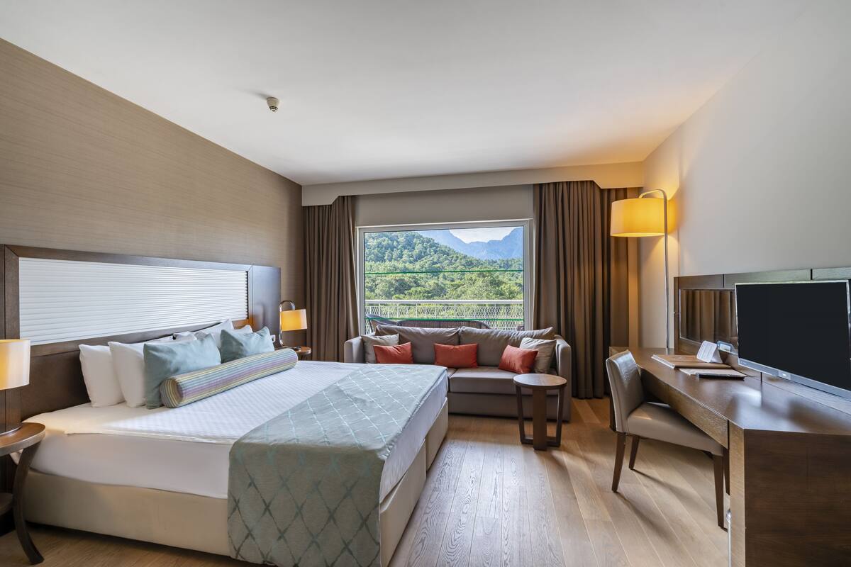 A hotel room with a bed, a sofa, a desk, and a TV.