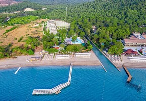 An aerial view of a coastal resort with a pier, beachfront villas, and a pool area.