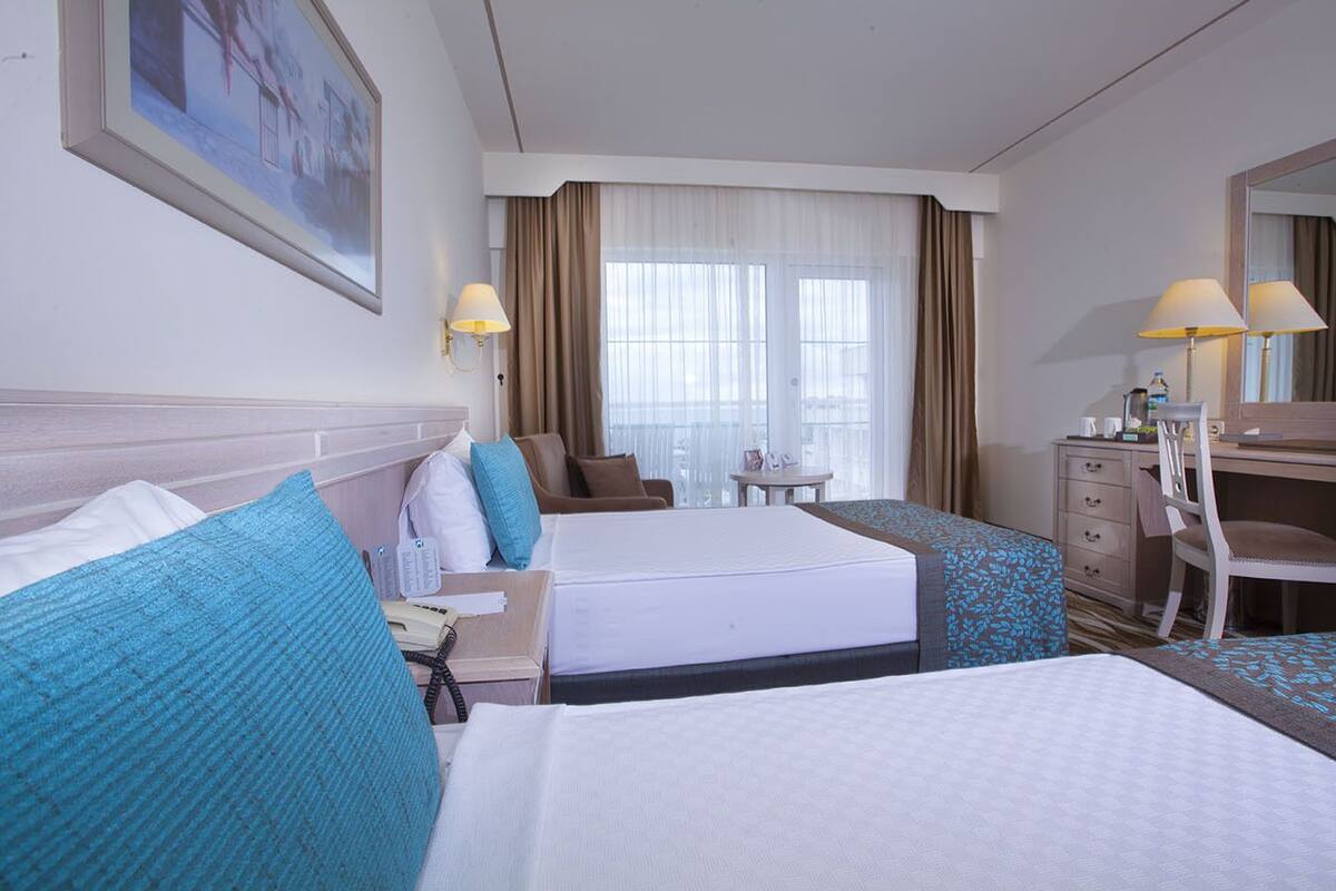 A hotel room with two beds, a desk, a chair, a small table, and a window with curtains.