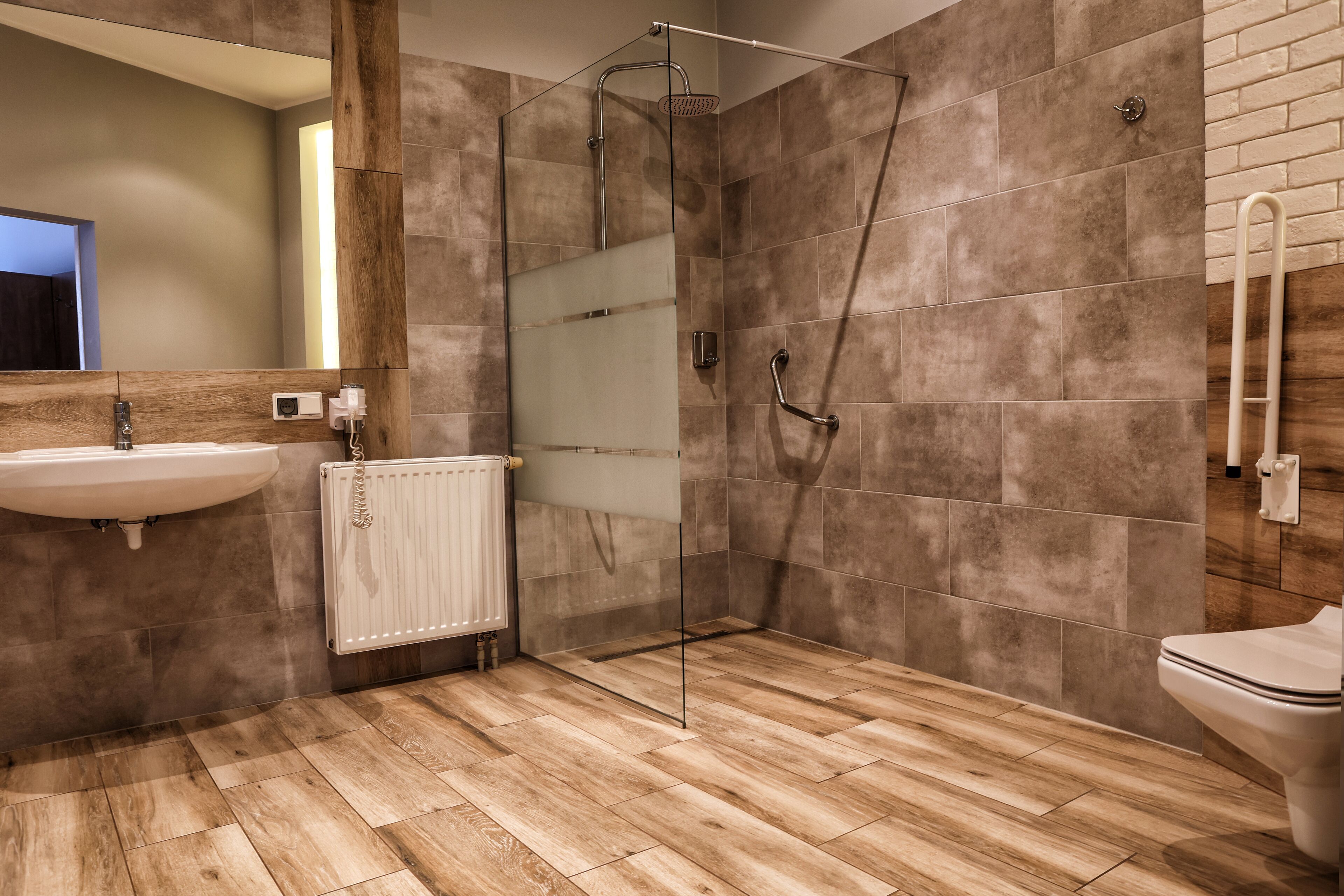 A modern bathroom with a glass shower enclosure, a wooden floor, a white sink, and a toilet.