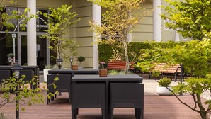 An outdoor patio area with black wicker furniture, potted plants, and a wooden bench. - Jan Sander Hotel (Aleksandrow Lodzki)