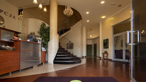 A reception area with a reception desk, a staircase, and a chandelier. - Jan Sander Hotel (Aleksandrow Lodzki)