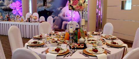 Un salón de banquetes con mesas redondas dispuestas para un evento formal, con manteles blancos, cubertería y centros de mesa florales.