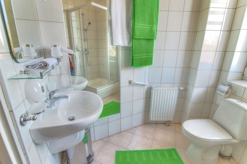 A bathroom with a sink, toilet, shower, and a towel rack with green towels.