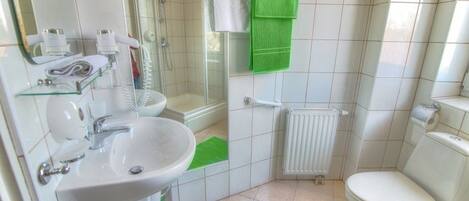 A bathroom with a sink, toilet, shower, and a towel rack with green towels.
