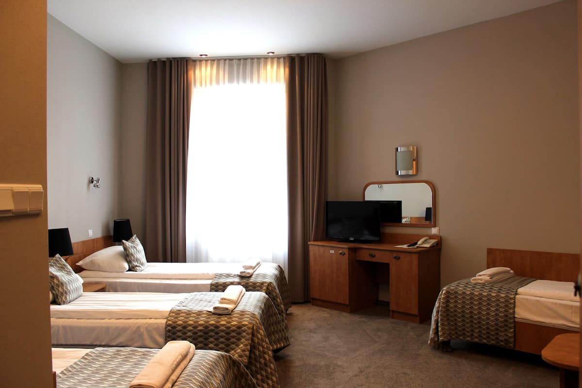 Quarto de hotel com duas camas, uma escrivaninha com televisão e uma janela grande com cortinas.