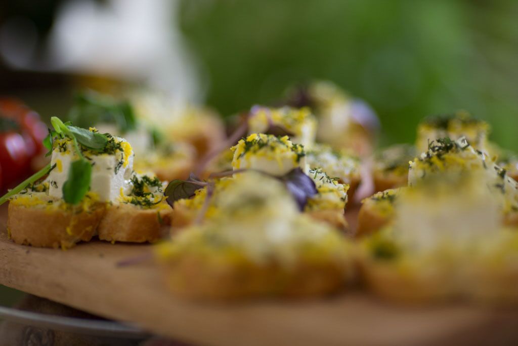 Puinen tarjoilulauta, jonka päällä on useita bruschetta-leipiä, jotka on koristeltu yrteillä ja juustolla.