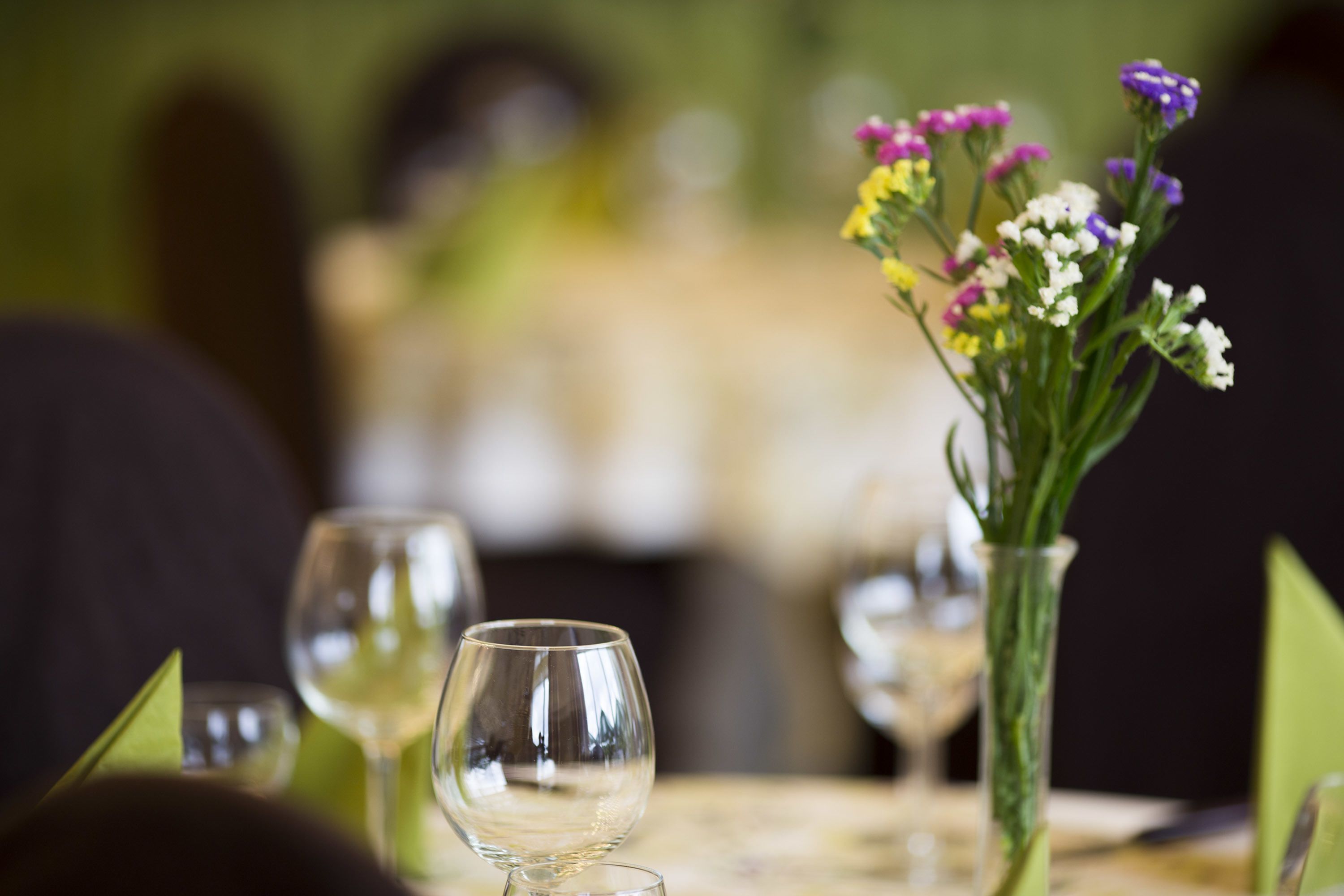 A dining table with a vase of flowers and wine glasses.