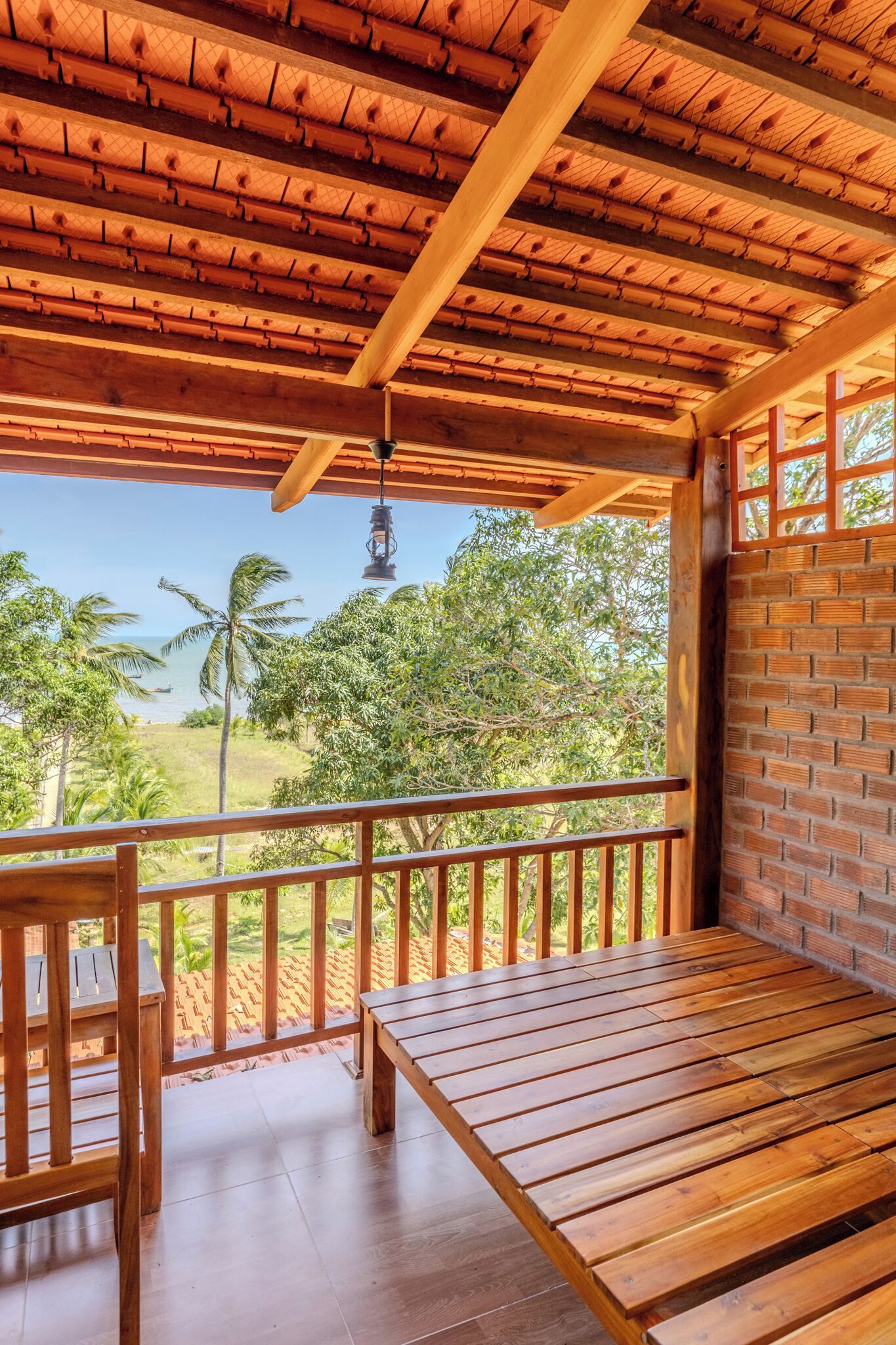 Eine Holzterrasse mit einer Bank und einem Tisch, mit Blick auf eine üppige Landschaft mit Palmen und Meer.