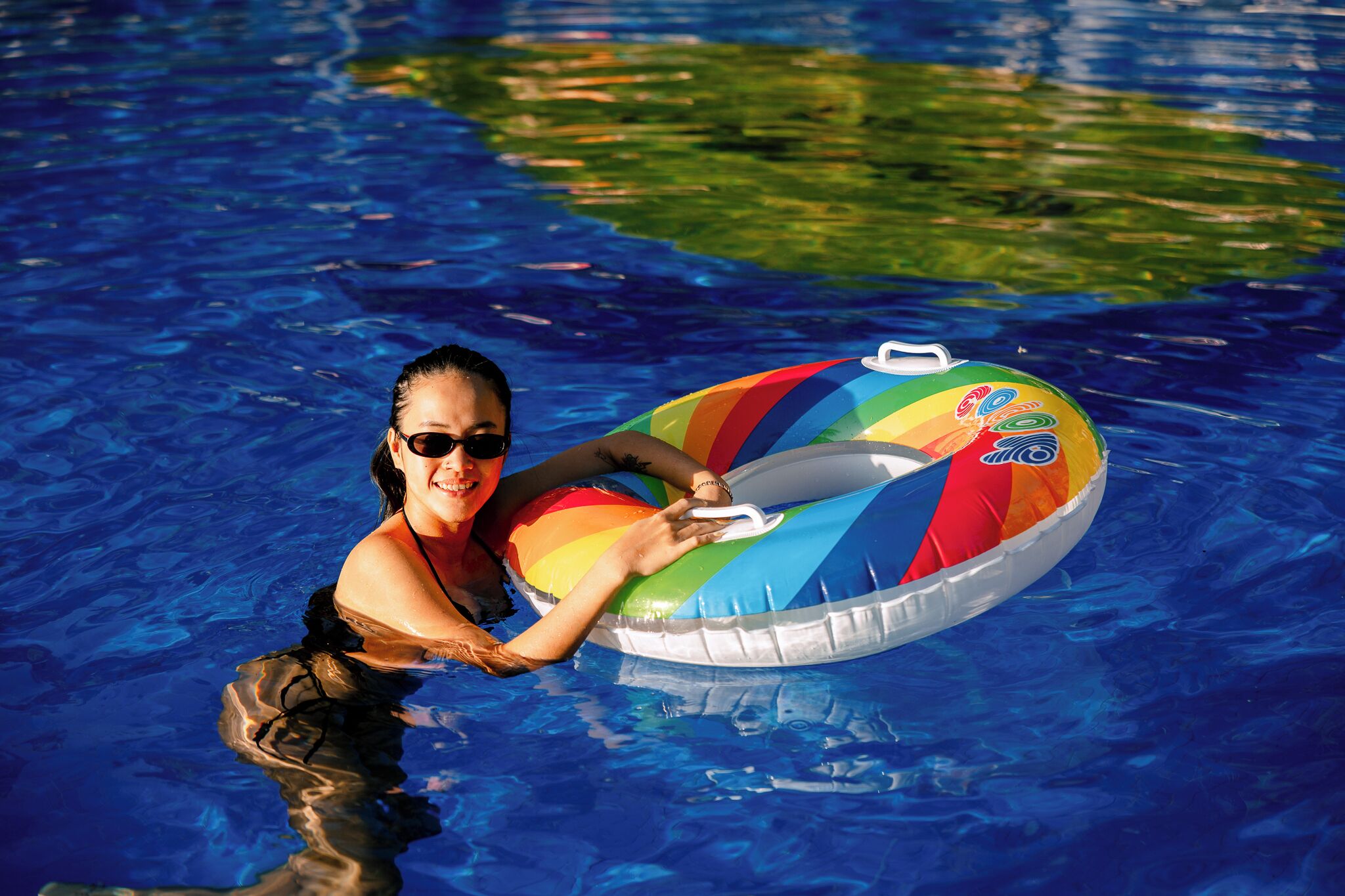 A person in a swimming pool holding a colorful inflatable ring.