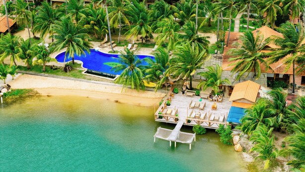 Een resort met een helderblauw zwembad, een houten terras en palmbomen.