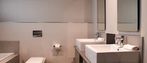 Un baño moderno con bañera, dos lavamanos y un inodoro.
