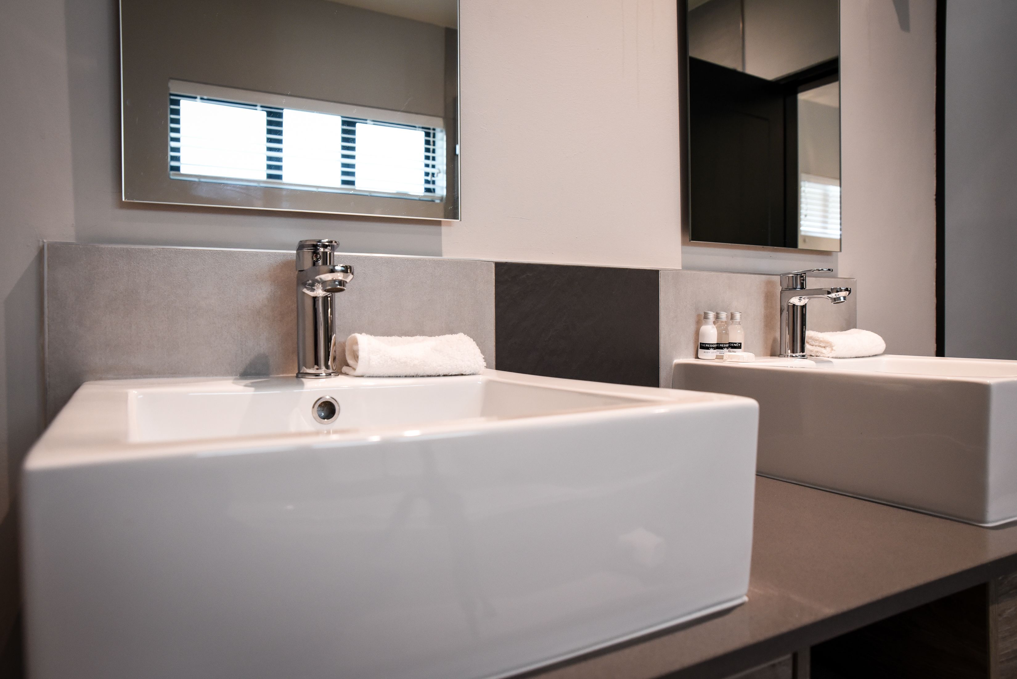 A modern bathroom with two white sinks, a large mirror, and a towel rack.