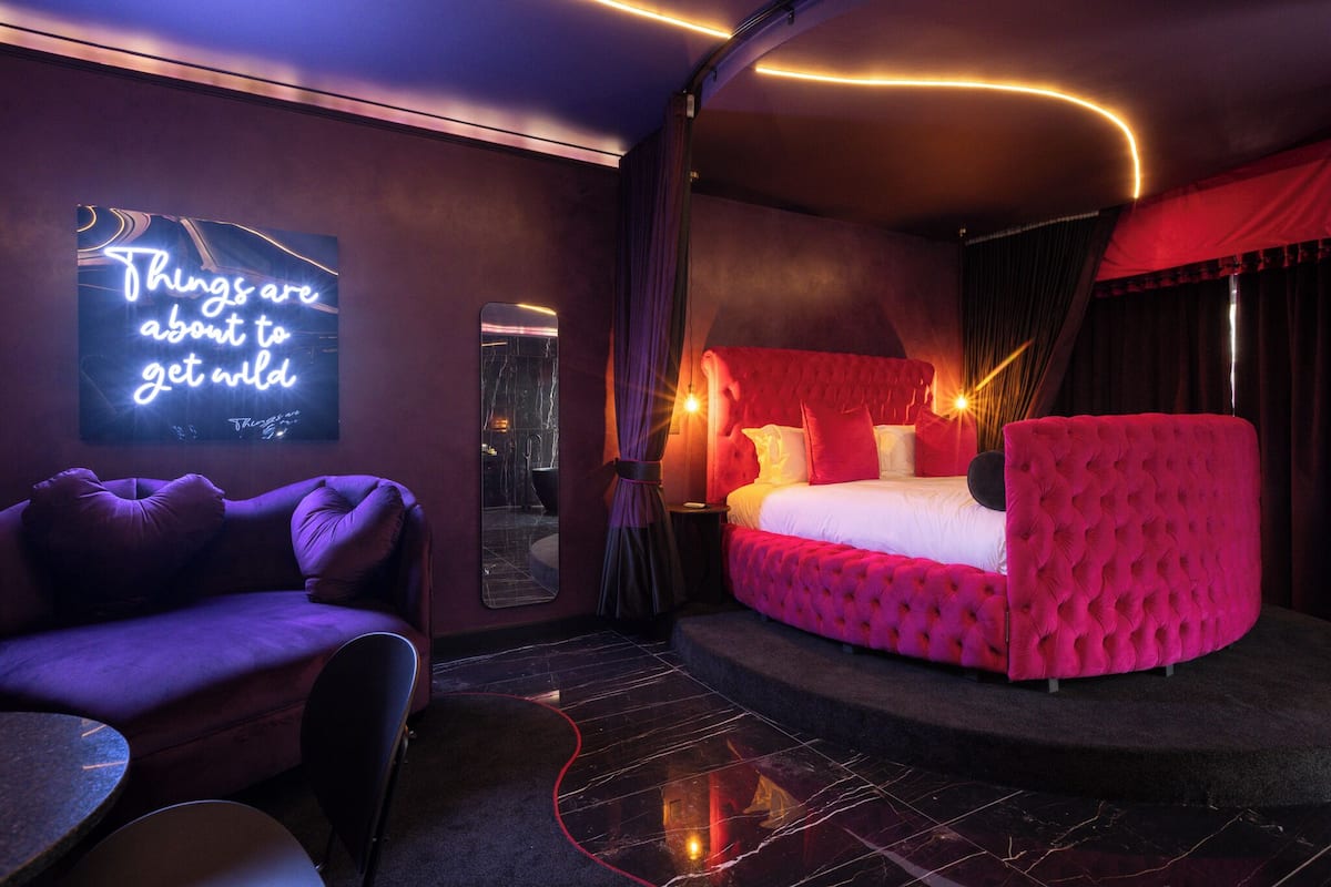 A modern hotel room with a large bed, a sofa, and a neon sign.