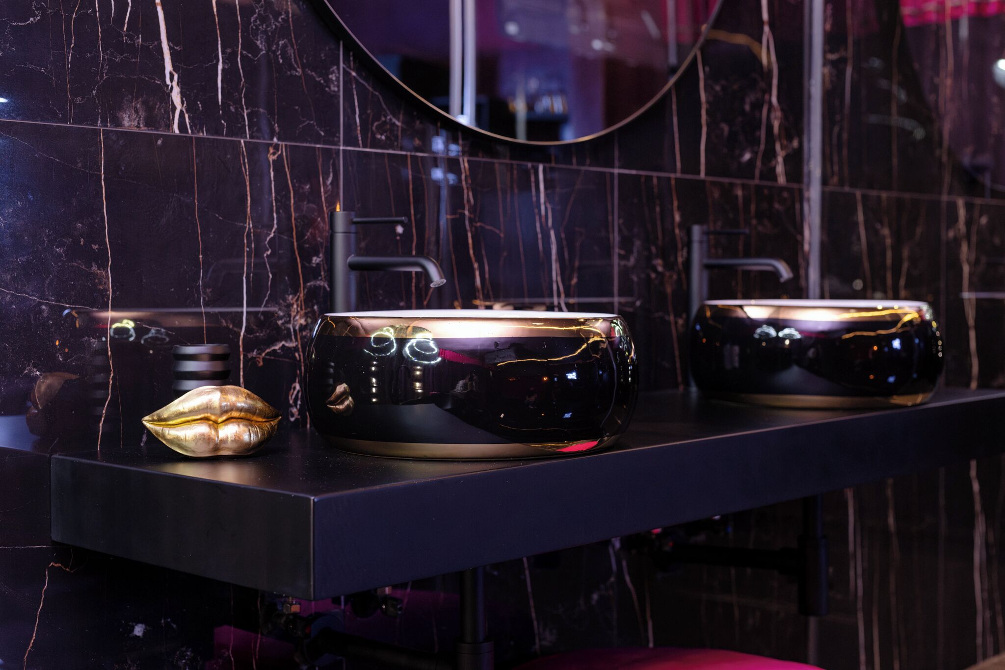A modern bathroom with a black marble backsplash, a sleek black sink, and a gold decorative object on the countertop.