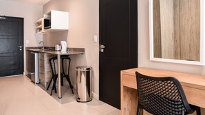 A compact kitchen with a black door, a white cabinet, a stainless steel trash bin, and a wooden table with a black chair.