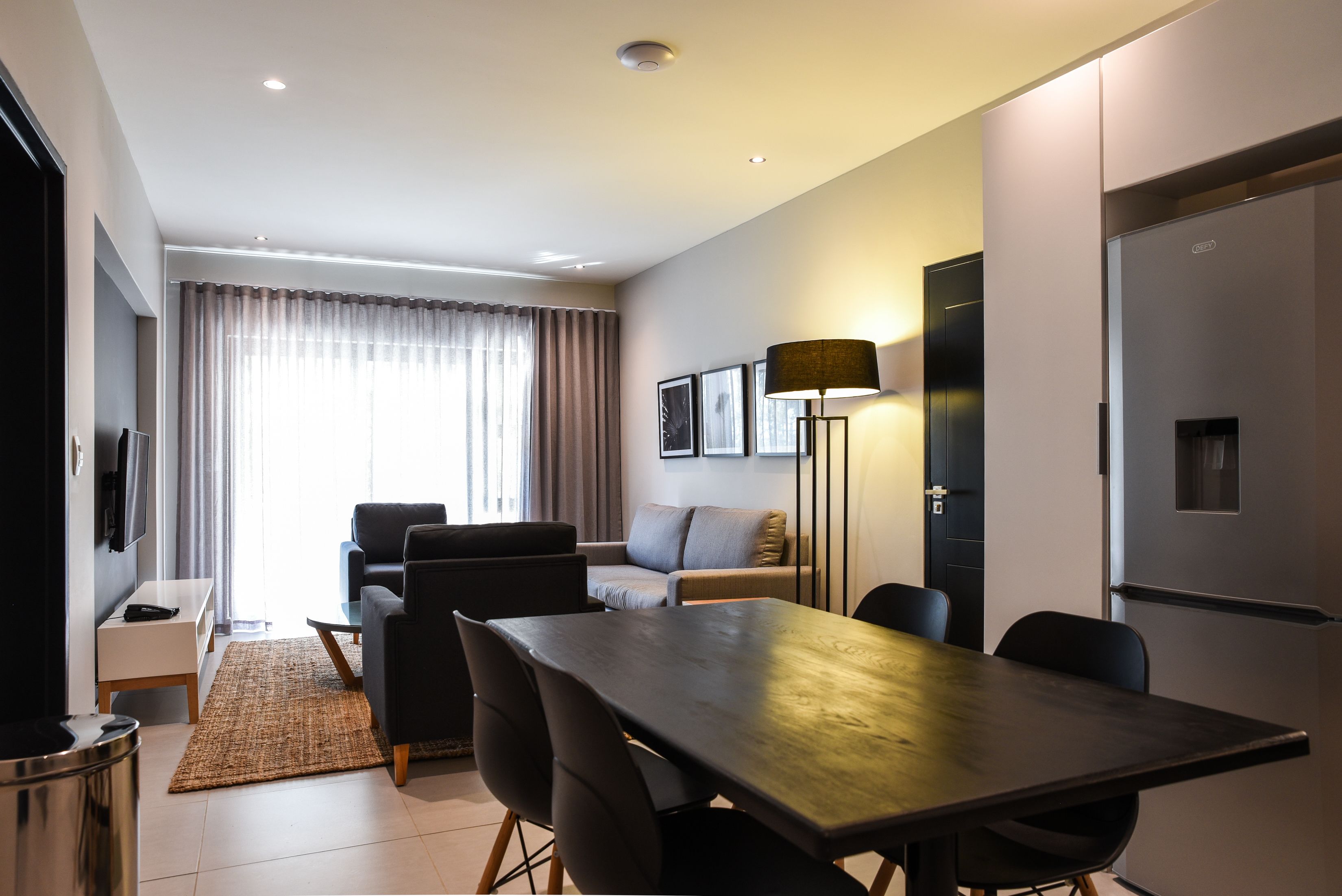 Ein modernes Wohnzimmer mit einer Couch, einem Esstisch mit Stühlen, einer Lampe und einem Fernseher.
