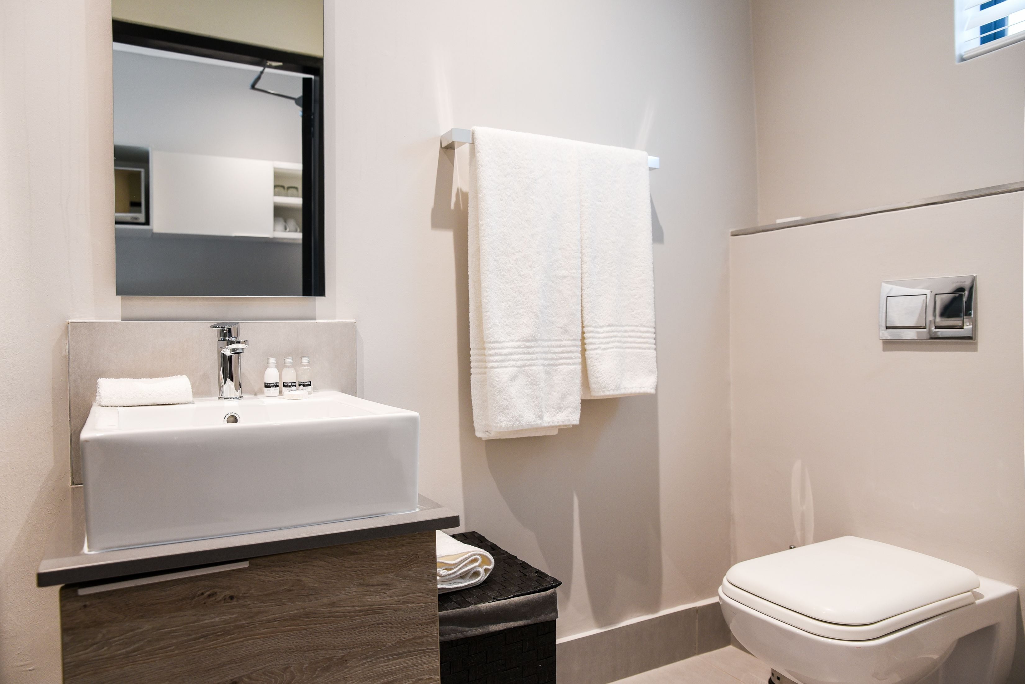 A modern bathroom with a white sink, mirror, and toilet.