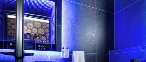Une salle de bain moderne avec des carreaux bleu foncé, un grand miroir, un lavabo rond et des toilettes.