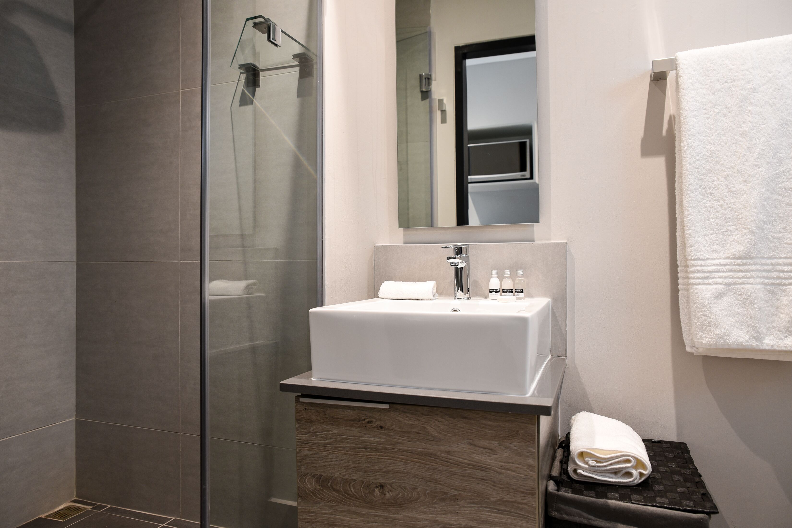 A modern bathroom with a glass shower enclosure, a white sink, and a wooden vanity.