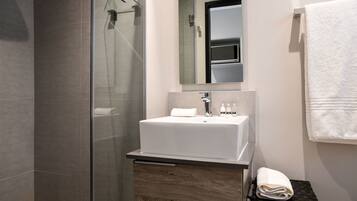 Un baño moderno con cabina de ducha de vidrio, un lavamanos blanco y un mueble de tocador de madera.
