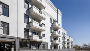 A modern multi-story residential building with balconies, large windows, and a flat roof.