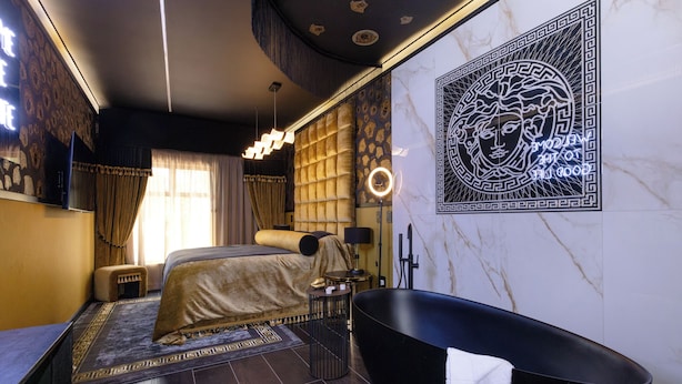 A modern bedroom with a large bed, a black bathtub, and a decorative wall piece.