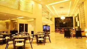 A spacious hotel lobby with a high ceiling, modern lighting, and a large television screen. - The Flora Grand (Vasco da Gama)