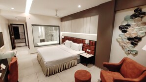 A modern hotel room with a large bed, a desk with a chair, a small round stool, and a seating area with a chair. - The Flora Grand (Vasco da Gama)