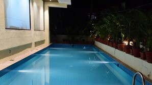 A swimming pool with a tiled edge, surrounded by potted plants and a wall. - The Flora Grand (Vasco da Gama)