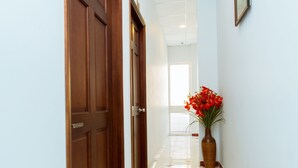 A hallway with wooden doors, a tiled floor with red accents, and a vase with red flowers. - Hotel Kim Yen (Ho Chi Minh City)