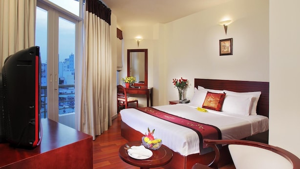 A hotel room with a bed, a desk, a chair, a TV, and a view of the city. - Hotel Kim Yen (Ho Chi Minh City)