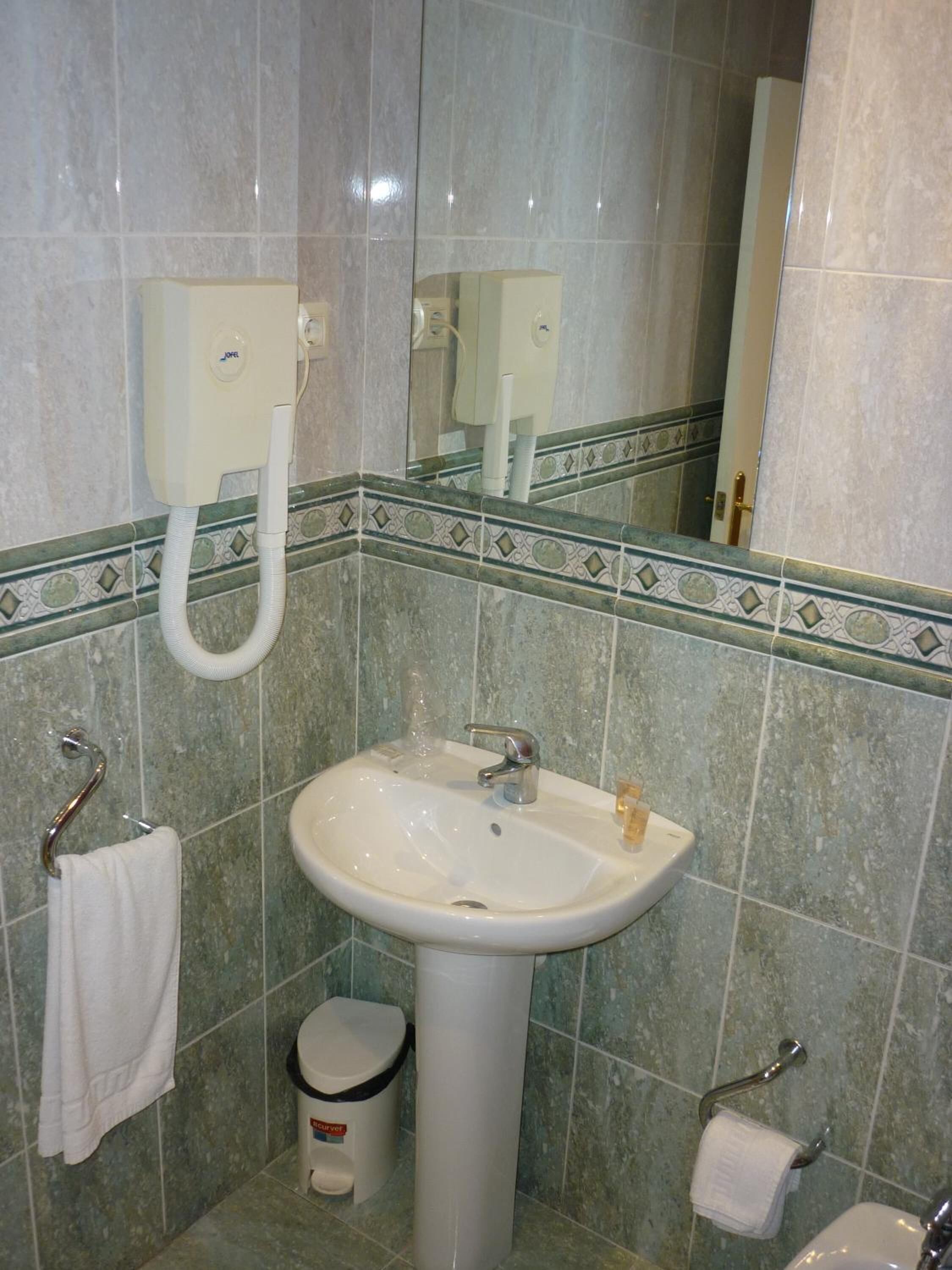 A bathroom with a pedestal sink, a mirror, a towel rack, and a trash bin.