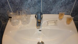 A white bathroom sink with a single faucet, surrounded by toiletries including a bottle of lotion and a small bottle of shampoo. - Hotel Tuto (Torrevieja)