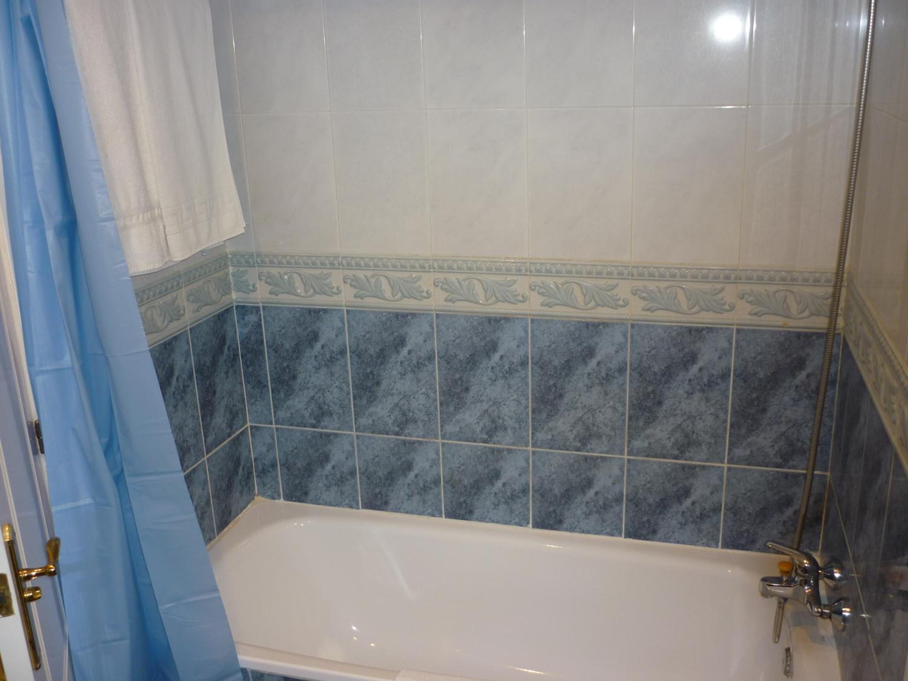 A bathroom with a bathtub, blue and white tiles, and a shower curtain.