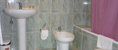 Une salle de bain équipée d’un lavabo sur colonne, d’un bidet, de toilettes et d’une poubelle.