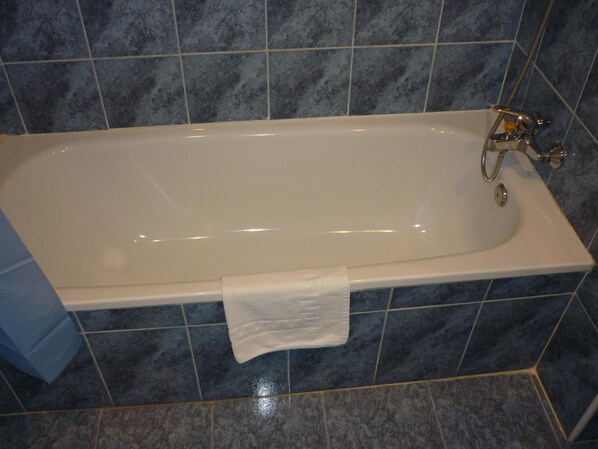 Una bañera blanca con cabezal de ducha y una toalla en el suelo.